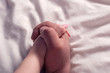 close up hands of loving couple lying on white bed sheet together