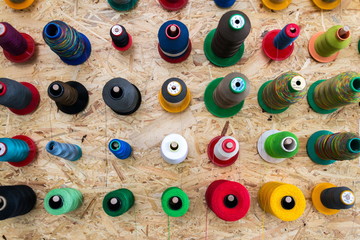 Wall Mural - Colorful thread reels on wooden wall set up for sewing machine, textile industry factory concept