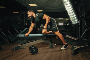 Muscular young man lifting weights in a dark gym