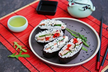 Assorted sushi sandwiches onigirazu with baked duck, spinach and sweet pepper and with salmon and cream cheese on a brown clay plate on a dark concrete background. Japanese food.