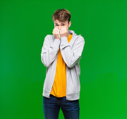 Wall Mural - young blonde man looking worried, anxious, stressed and afraid, biting fingernails and looking to lateral copy space against chroma key wall