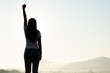 Woman with fist in the air during sunset sunrise mountain in background. Stand strong. Feeling motivated, freedom, strength and courage concept.