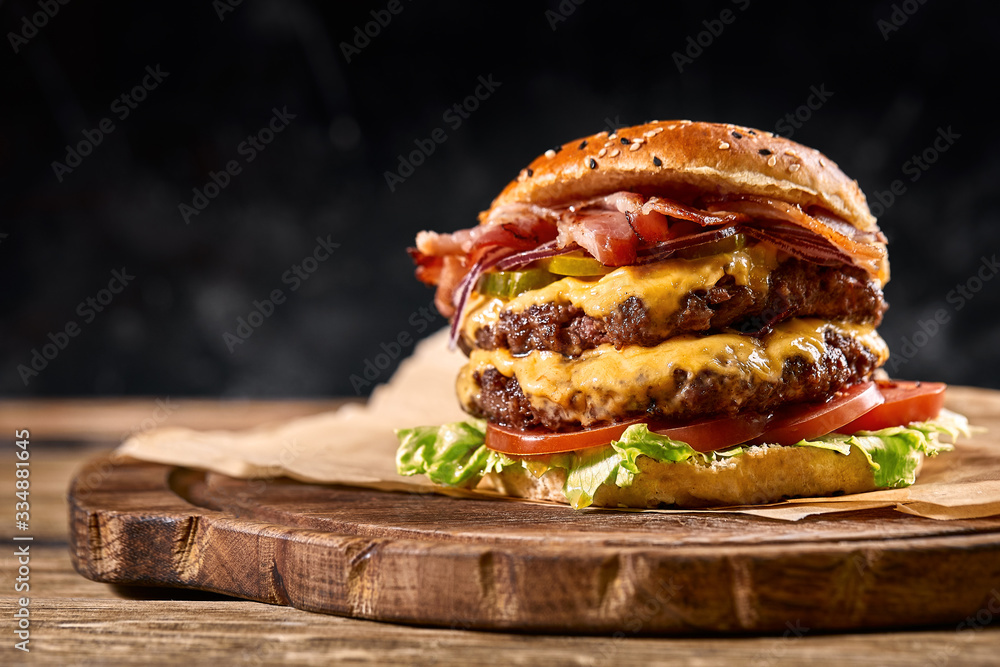 Juicy American burger, hamburger or cheeseburger with two beef patties, with sauce and basked on a black background. Concept of American fast food. Copy space - obrazy, fototapety, plakaty 