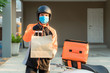 Delivery Asian man wear protective mask in orange uniform and ready to send delivering Food bag in front of customer houes with case box on scooter, express food delivery and shopping online concept..