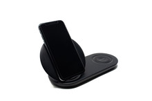 Wireless Qi charger with a black cell phone standing on its base. Isolated on a white background.