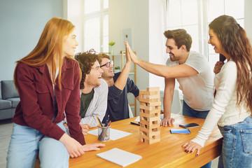 A group of young people play board games give five sitting at a table in the room.