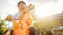 Musician Man Using A Bow To Practicing The Cello Playing With The Melodiousness At The Sunset. Selected Focus.