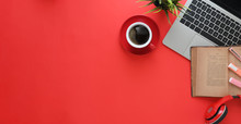 Top View Image Of Computer Laptop Putting On Red Working Desk With Wireless Headphone, Old Book, Coffee Cup, Potted Plant. Colorful Workspace Concept.