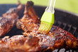 cooking, culinary and food concept - close up of brush smearing marinade sauce on barbecue meat roasting on brazier grill outdoors