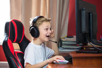 cute boy looks at the monitor and plays a computer game with headphones at the table