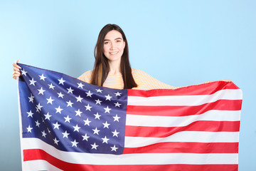 Beautiful young girl holding the flag of America on a colored background.