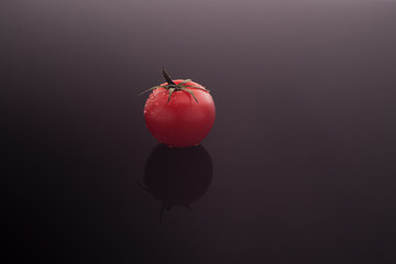 A small cherry tomato in dewdrops on a dark gray gradient background.