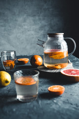 Wall Mural - Citrus tea in a transparent teapot on a dark concrete background. Healthy drink, vegan, eco product.