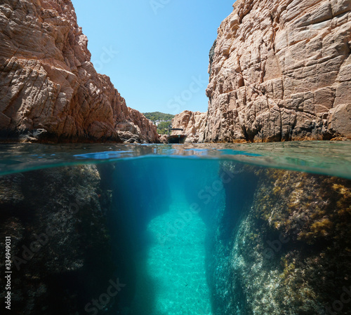 Fotomural Boat in a narrow passage on rocky coast, split view over and under water surface