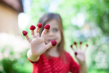 Young girl is holding raspberries on her fingers, outdoor shoot