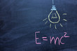 Well-known physical formula. E=mc2 on a chalk Board. Drawing of a light bulb. The concept of a sudden idea