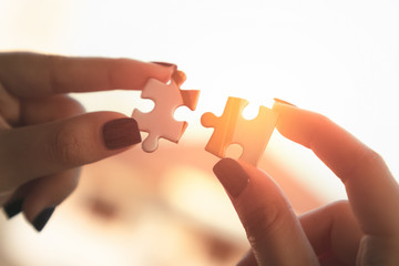 Hands of a woman hands holding two pieces of a puzzle in front of the sun with lens flare.