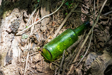 An Empty Green Glass Bottle Lays Discarded On The Ground In The Woods.