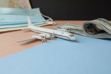 A Toy Plane On The Background Of Dollar Bills, A Map And A Face Mask, The Concept Of Closing Borders Around The World Due To Coronavirus, Financial Losses Of Airlines And Tour Operators.