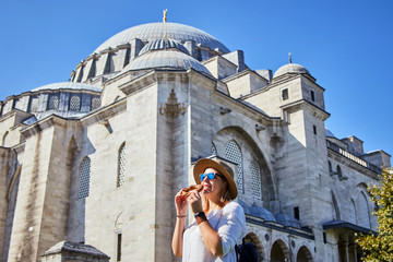 Wall Mural - Happy attractive woman tourist in hat, eating Simitci (a round bagel with sesame seeds) against the background of Suleymaniye mosque, Istanbul,Turkey. Religion and travel concept.