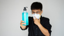 The Young Man Wearing Face Hygienic Mask. Close Up Isolated Hand Show Blue Pump Liquid Alcohol, Antiseptic For Sanitize,protect People From Coronavirus Disease Covid-19. Man And Women Protective Dange