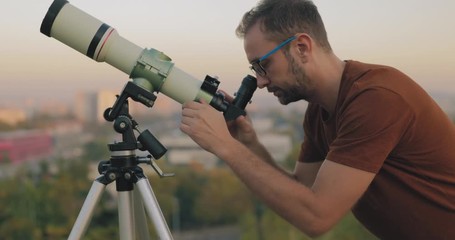Wall Mural - astronomer with a telescope watching at the stars and moon with blurred city background.