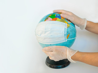 Earth globe dressed in a protective mask on the hands of a man in protective gloves. Symbol that people all over planet are quarantined due to epidemic and pandemic of Coronavirus. White background.