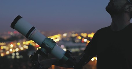 Wall Mural - astronomer with a telescope watching at the stars and moon with blurred city lights in the backgroun