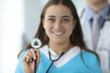 © H_Ko - Close-up of female hand holding stethoscope with cannabis symbol. Cheerful smiling nurse in medical uniform in clinic. Healthcare and medical marijuana concept