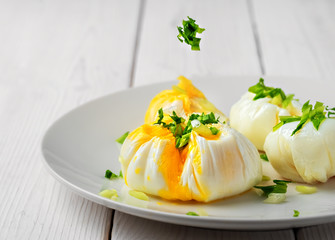 Eggs - poached decorated with fresh herbs on a white plate, close-up, shallow depth of field. The idea of making a healthy breakfast or lunch with organic products.