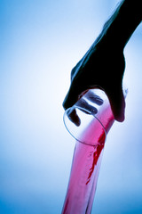 Wall Mural - Hand holding a plastic glass with a red juice splash on a blue background