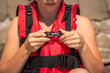 Young girl putting on red life jacket on the beach on a summer sunny day. Female hands fastens plastic buckle clasp of life vest. Safety during water sports