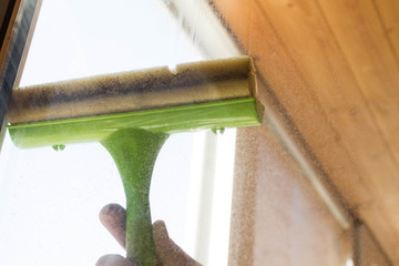 Wall Mural - Washing plastic Windows in the house. Window cleaning tool in the hand of a man washing a dirty window on a balcony close-up