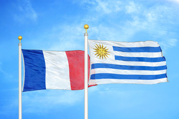 france and uruguay two flags on flagpoles and blue cloudy sky