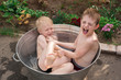 Two brothers bathe in basin outdoors. Siblings play splash
