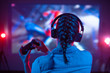 Girl in headphones plays a video game on a screen projector or TV in the dark room. Gamer with a joystick. Online games with friends, competitions. Fun entertainment. Teenagers play arcade. Back view