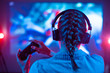 © Anton - Girl in headphones plays a video game on a big screen projector or TV in a dark room. Gamer with a joystick. Online games with friends, competitions, wins. Fun entertainment. Teenagers play strategy