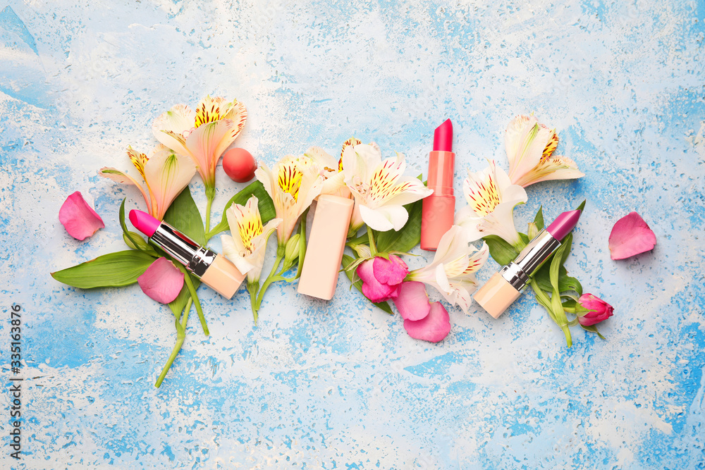 Different lipsticks and flowers on color background