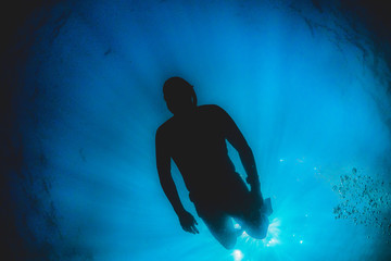 Silhouette of a free diver swimming down into the blue water