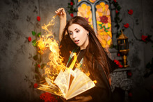 A Young Woman In A Black Mantle With A Striped Scarf Around Her Neck Casts A Spell From A Book And Conjures With A Wand Of Magic.