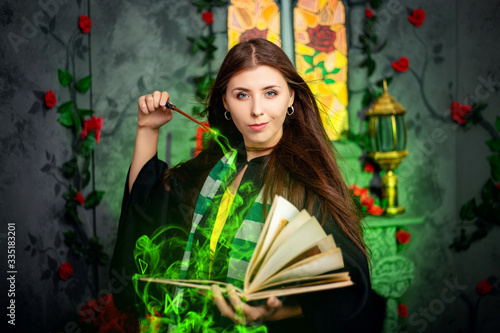 Fotografía A young woman in a black mantle with a striped scarf around her neck casts a spell from a book and conjures with a wand of magic