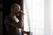© JLSanchezM - Man locked up at home. Looking out the window and drinking coffee. Covid coronavirus quarantine