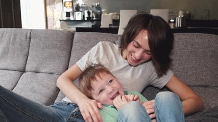 pretty mother is playing with her son on a sofa at home. the parent is spending quarantine at home w