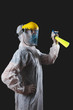 Person with protective antiviral mask, suit, helmet and chemical decontamination sprayer bottle in home isolation.