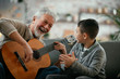 © JustLife - Grandpa and grandson playing guitar. Grandfather and grandson enjoying at home.