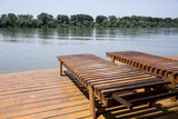 Fototapeta Pomosty - Two wooden sun loungers by the water