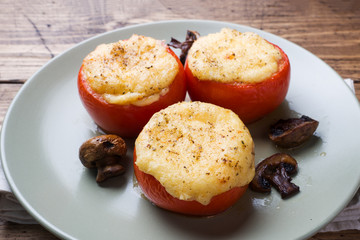 Wall Mural - Baked whole tomatoes stuffed with mushrooms and cheese with seasonings on a wooden background. Close up Selective focus