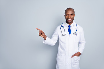 Wall Mural - Photo of cheerful doctor dark skin guy virologist family doc direct finger empty space advising use epidemic simple rules wear lab coat neck tie stethoscope isolated grey color background