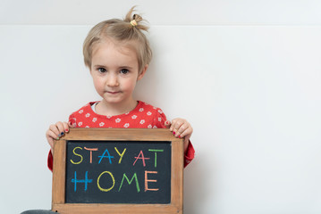 Portrait of girl while coronavirus and pandemic holding board with hashtag stay at home. Covid-19 and children in quarantine with copy space on a white background.