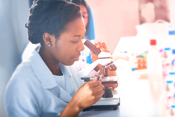 Young smart African female scientist, medic or tech evaluates patient samples through microscope in test lab. Histopathology, signs of pathology in patients with covid-19 pneumonia.